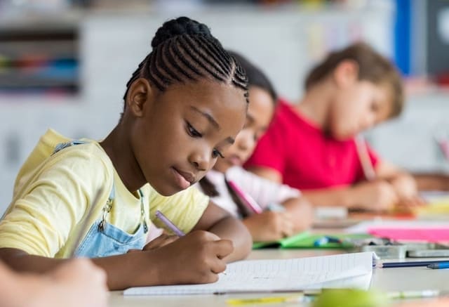 Leerling schrijft in haar schrift terwijl de rij naast haar doorwerkt